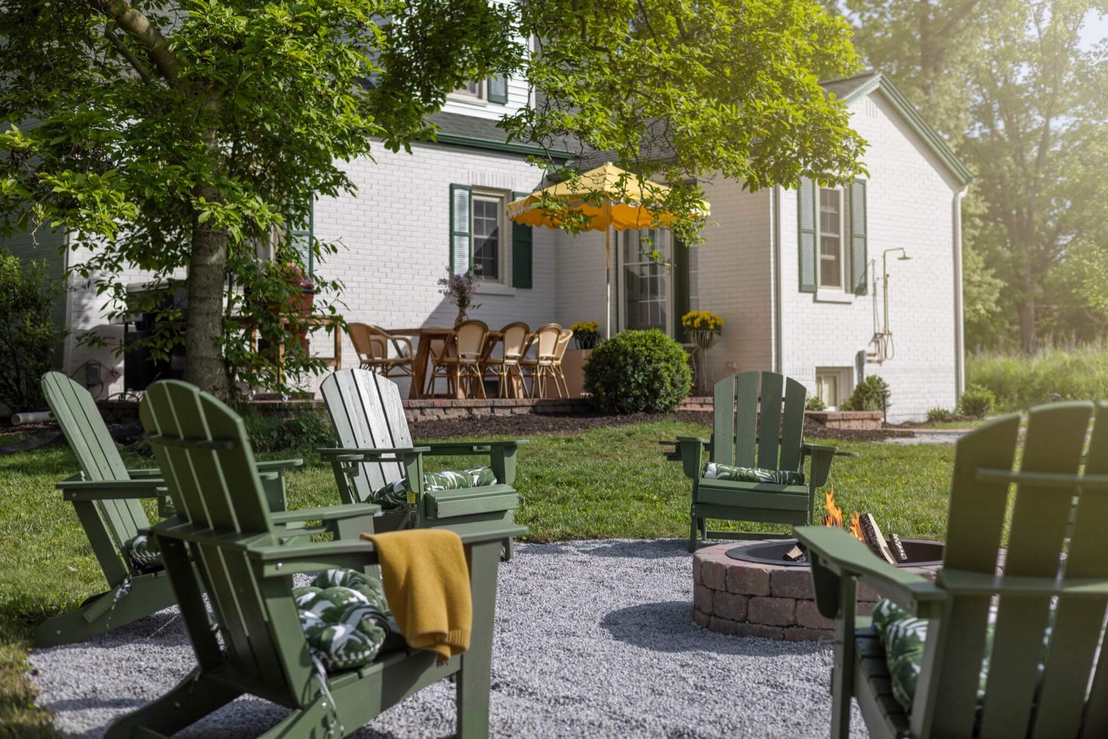 Green Adirondack chairs around the fire pit behind the white brick house